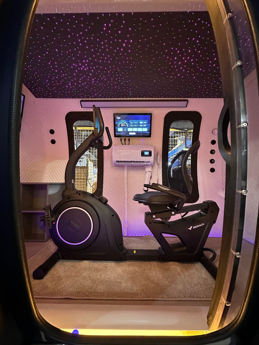 ExS64 exercise configuration framed through the doorway with upright and recumbent bikes lit by pink and purple ambient lighting beneath the starlight ceiling