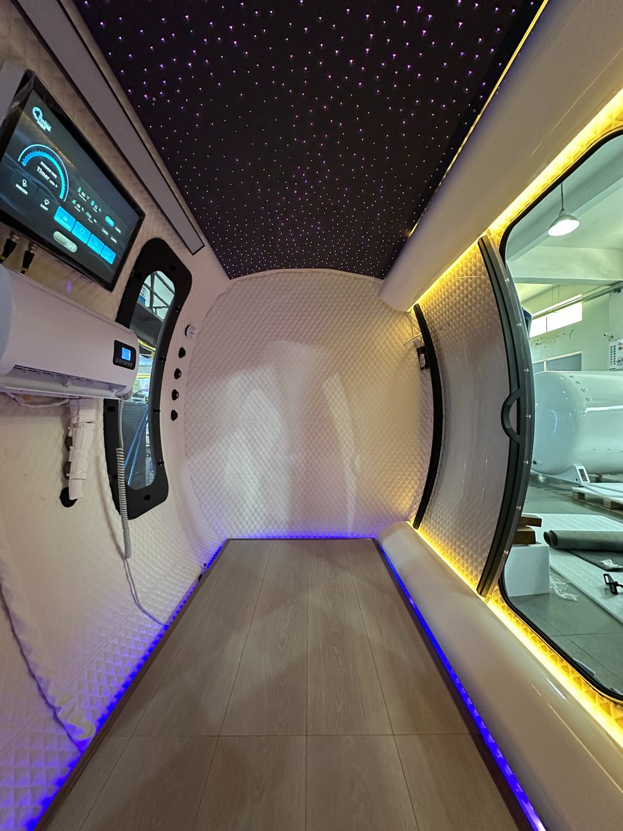 Full-length interior view of the ExS64 walk-in chamber showing the tiled floor, touchscreen and air-conditioning unit on the left wall, arched window, and blue and yellow LED lighting