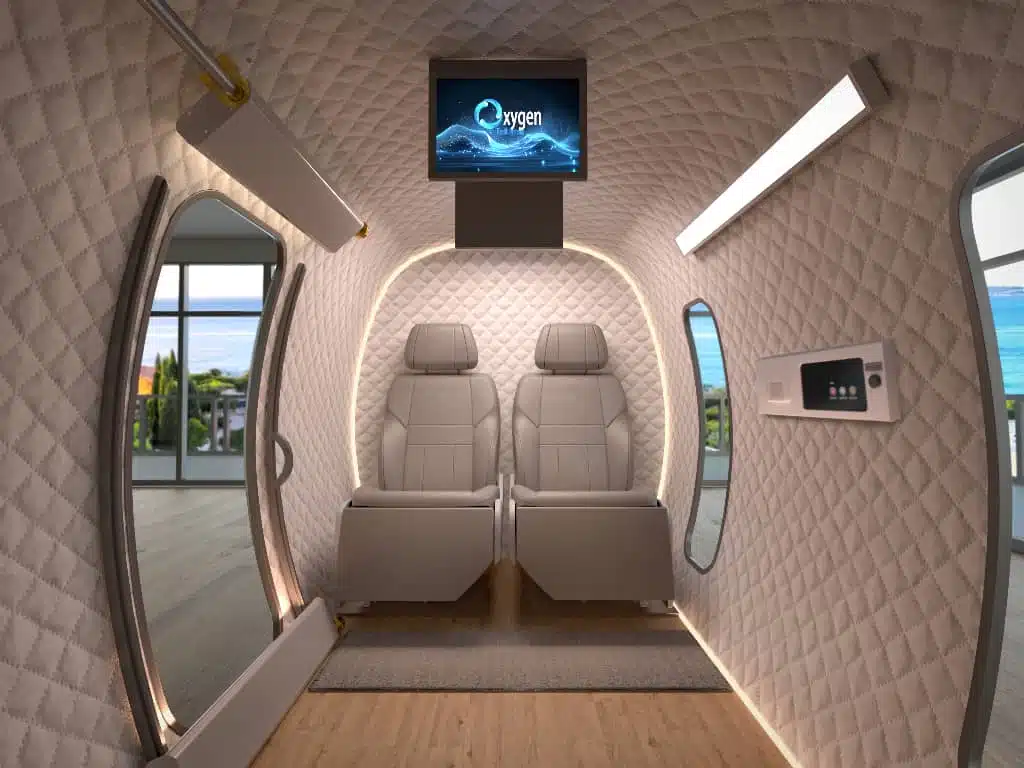 Rendered ExS64 interior configured with two cream airplane-style recliner seats, overhead TV, side control panel, and ocean-view windows